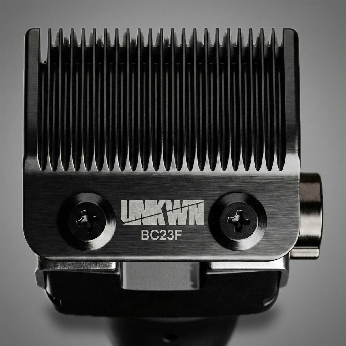 Close-up of the BC23F fade blade mounted on the UNKWN Vortex Cyclone Clipper, showing both mounting screws and the UNKWN mark